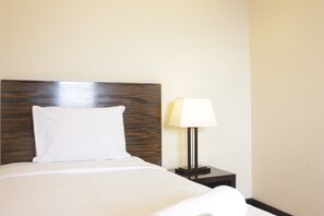 A neatly made bed with a wooden headboard, a bedside table with a lamp, and a plain wall. - Gorgeous & Comfy 2Br At Braga City Walk Apartment (Bandung)