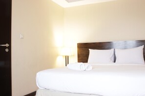 A neatly made bed with white linens and a folded towel, a wooden headboard, and a bedside lamp. - Gorgeous & Comfy 2Br At Braga City Walk Apartment (Bandung)