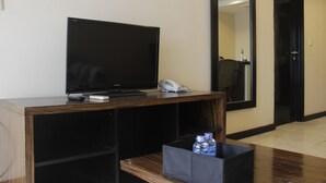 A hotel room with a flat-screen TV on a wooden console, a telephone, and a water bottle on a small table.
