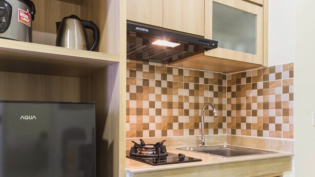 A kitchen with a black refrigerator, a stove, a sink, and a coffee maker on the countertop. - Luxurious 2Br At Meikarta Apartment (Cikarang)