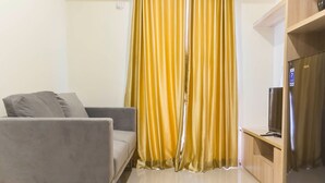 A modern living room with a grey sofa, a wooden cabinet with a television, and a yellow curtain. - Luxurious 2Br At Meikarta Apartment (Cikarang)