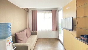 A compact living space with a sofa, a water dispenser, a television, and a window with curtains. - Relaxing 2Br Apartment At The Jarrdin Cihampelas (Bandung)