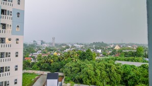 A high-rise building with multiple windows and balconies, overlooking a densely populated urban area with various buildings and greenery.