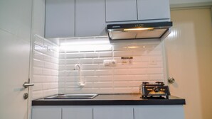 A compact kitchen with white cabinets, a black countertop, a built-in oven, and a wall-mounted exhaust hood.