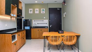 A compact kitchen with wooden cabinets, a black refrigerator, a built-in oven, and a dining area with wicker chairs.