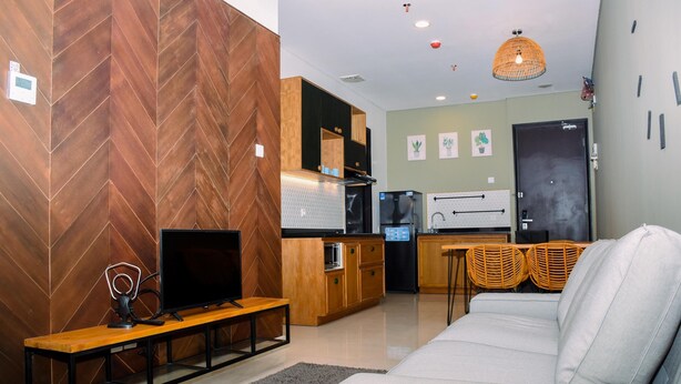 A modern living room with a sofa, a TV on a wooden stand, and a kitchen in the background.