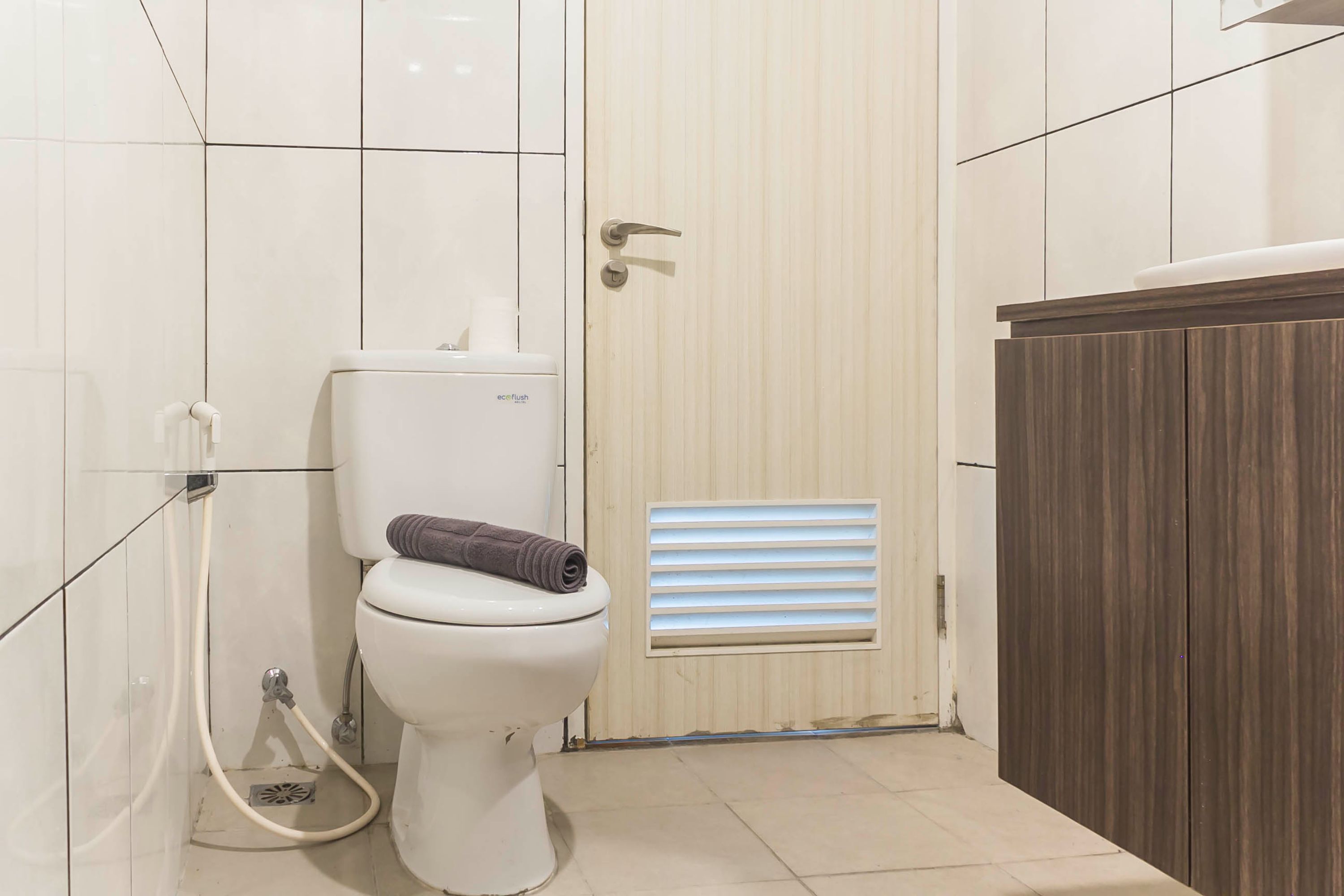 Une salle de bain équipée de toilettes, d’une serviette, d’un flexible de douche et d’une bouche d’aération.