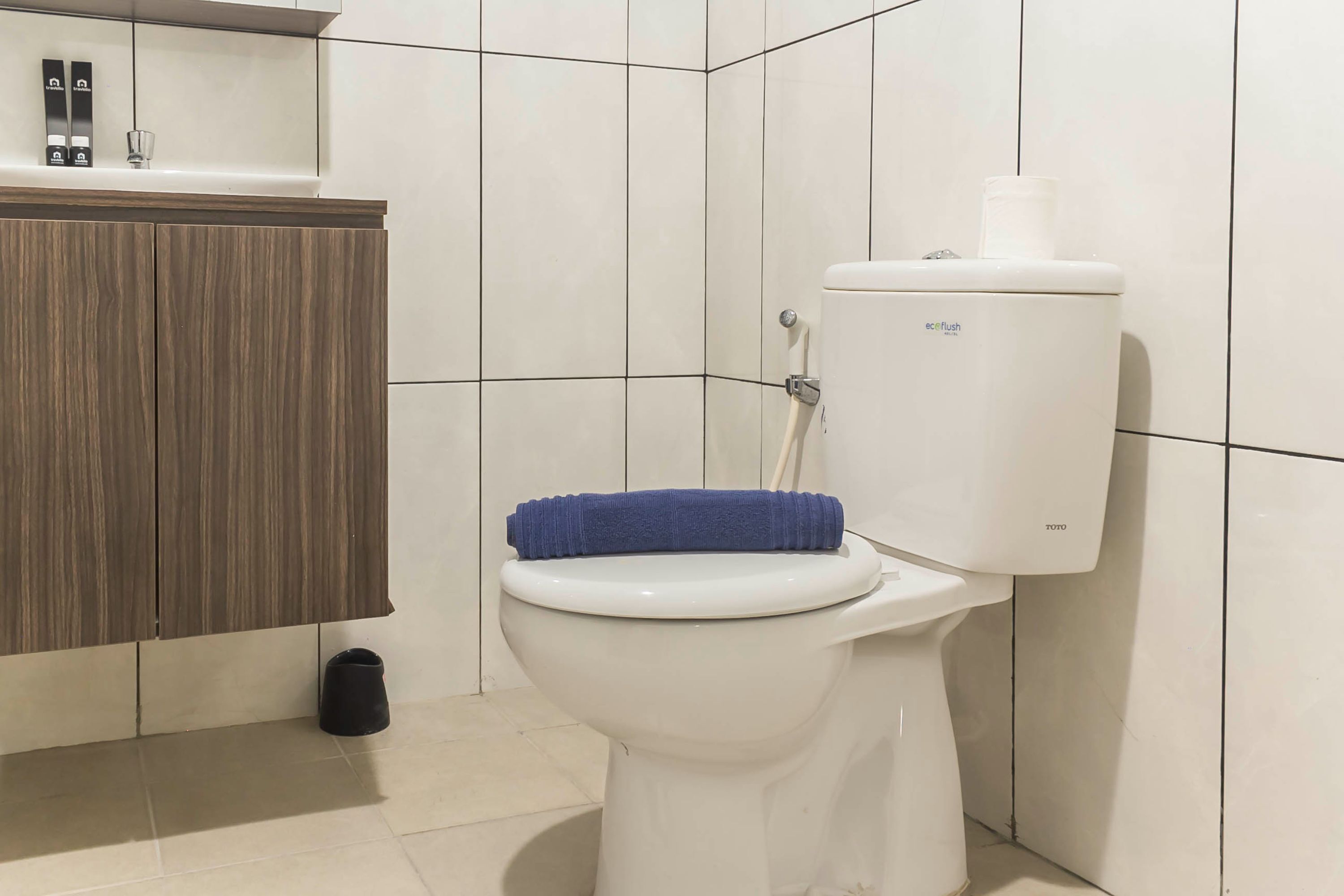 A white toilet with a blue towel on top, a wooden cabinet, and a black trash bin.