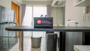 Ein Hotelzimmer mit Küchenzeile, einem Mülleimer, einem Stuhl, einem Tisch mit einer Tasche mit dem Aufdruck 'Travelio Property Management Complimentary Food & Beverage' und einem Telefon.