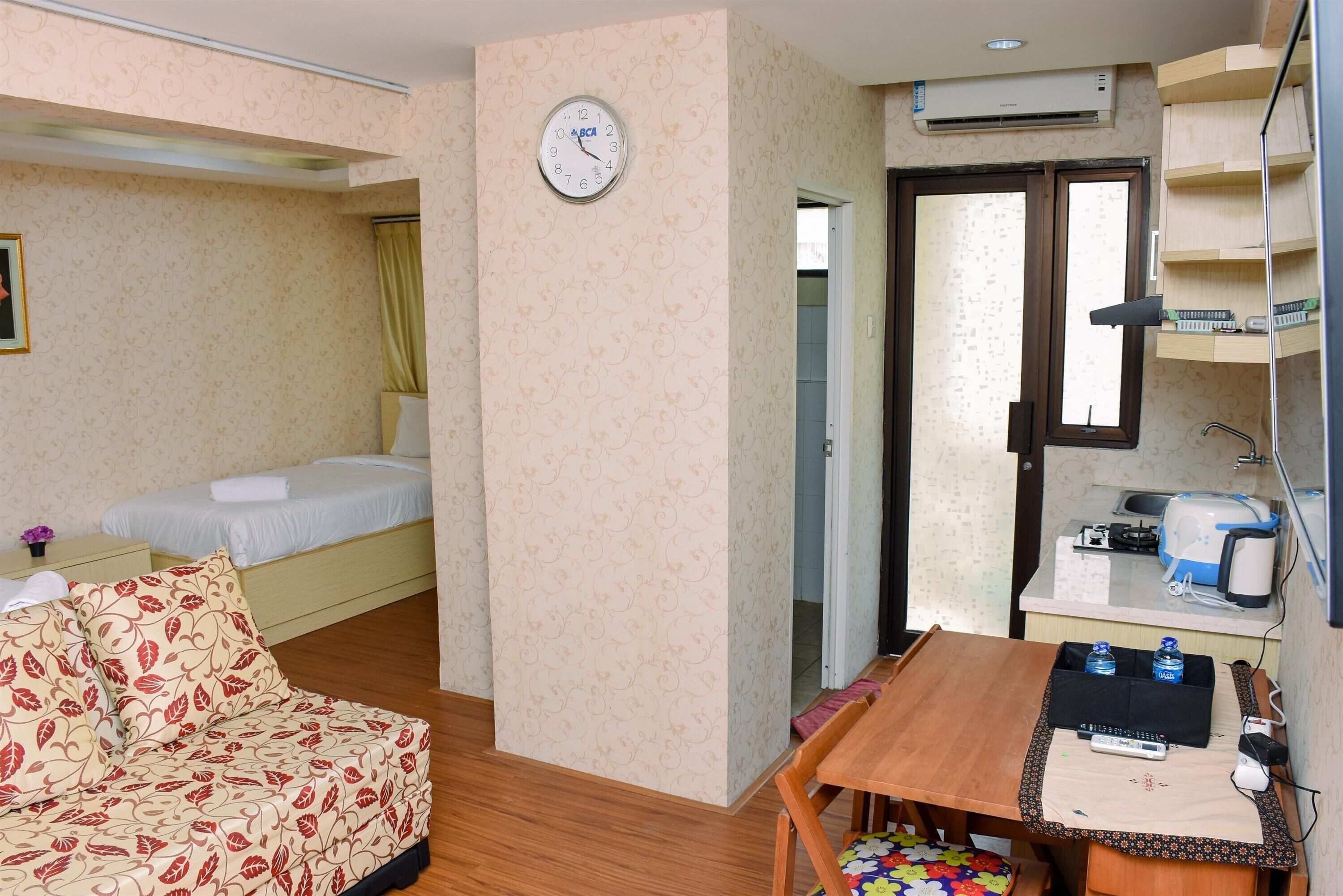 A compact hotel room with a bed, a sofa, a dining table, and a kitchenette.