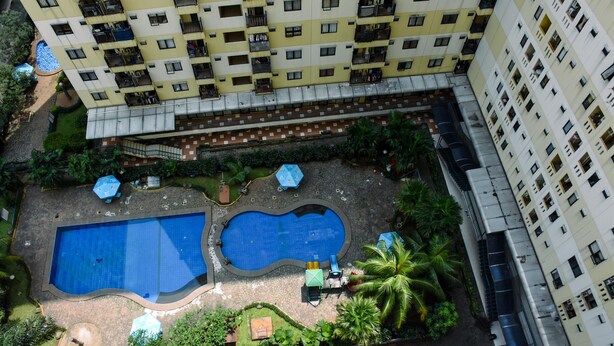 A high-rise building with multiple balconies, a swimming pool area with two pools, and surrounding greenery. - Comfort Living And Strategic Studio At Kebagusan City Apartment (Jakarta)