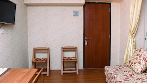 A room with a wooden table, two wooden chairs, a bed with patterned bedding, a television mounted on the wall, and a door with a handle. - Comfort Living And Strategic Studio At Kebagusan City Apartment (Jakarta)