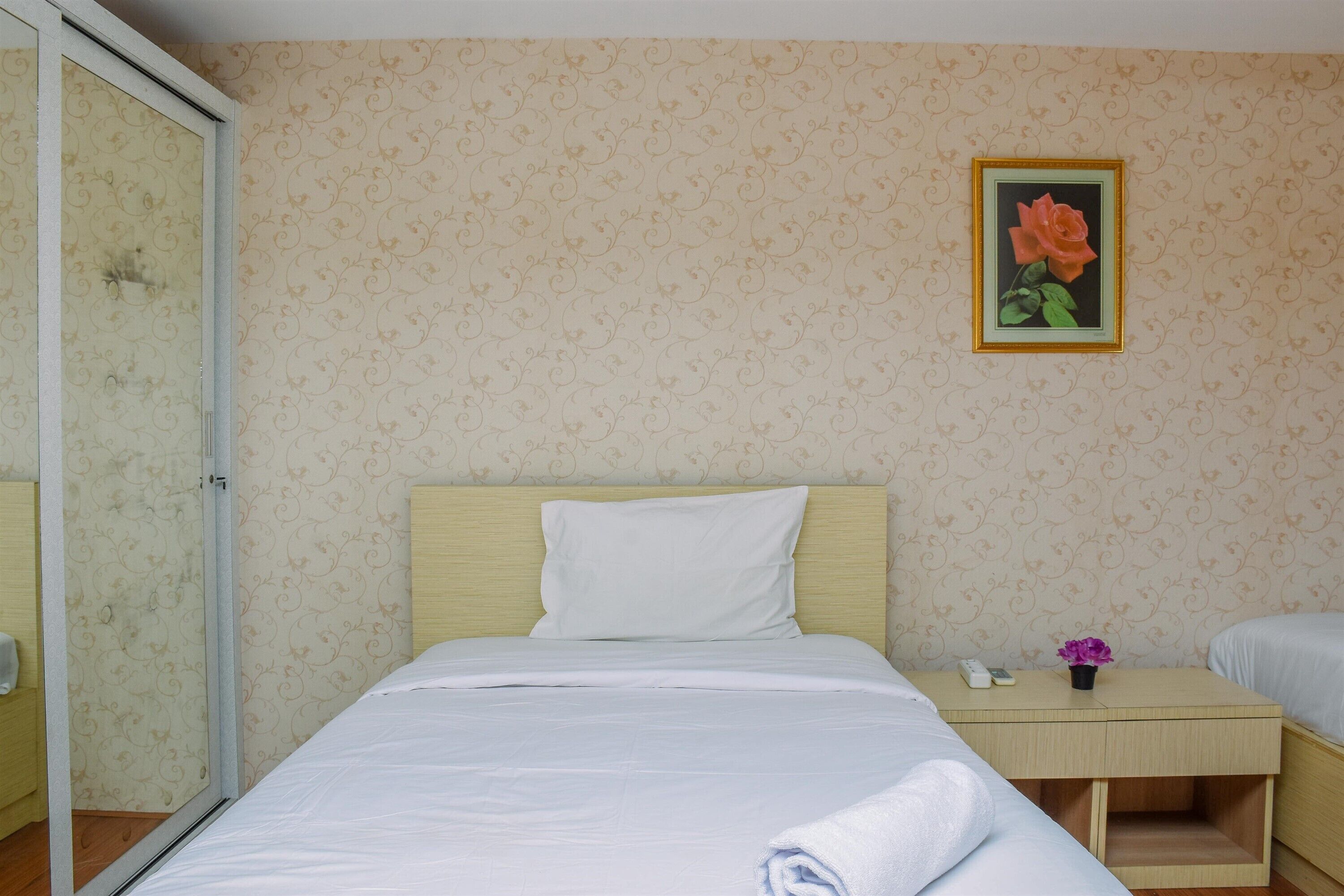 Habitación de hotel con cama, mesita de noche, un cuadro con una rosa y un espejo.