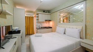 Una habitación de hotel con cama, televisor, escritorio, espejo y kitchenette.