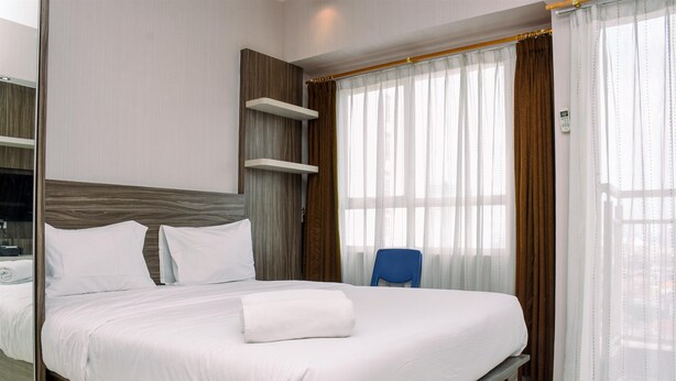 Una habitación de hotel moderna con una cama grande, cabecera de madera, estanterías empotradas, una silla azul y un amplio ventanal con cortinas.
