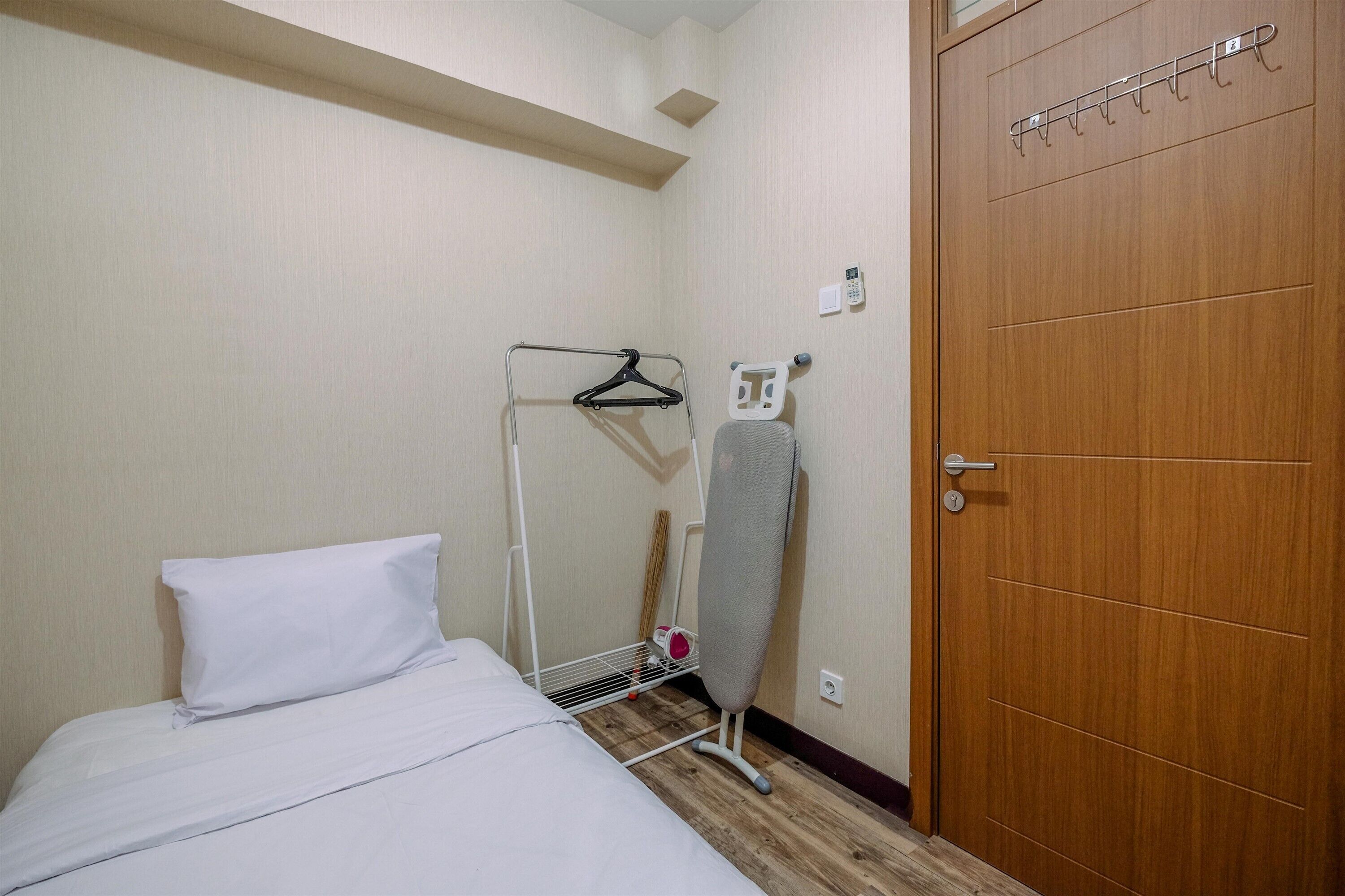 Una camera d'albergo con un letto, una porta in legno, un appendiabiti e un asse da stiro fissata al muro.