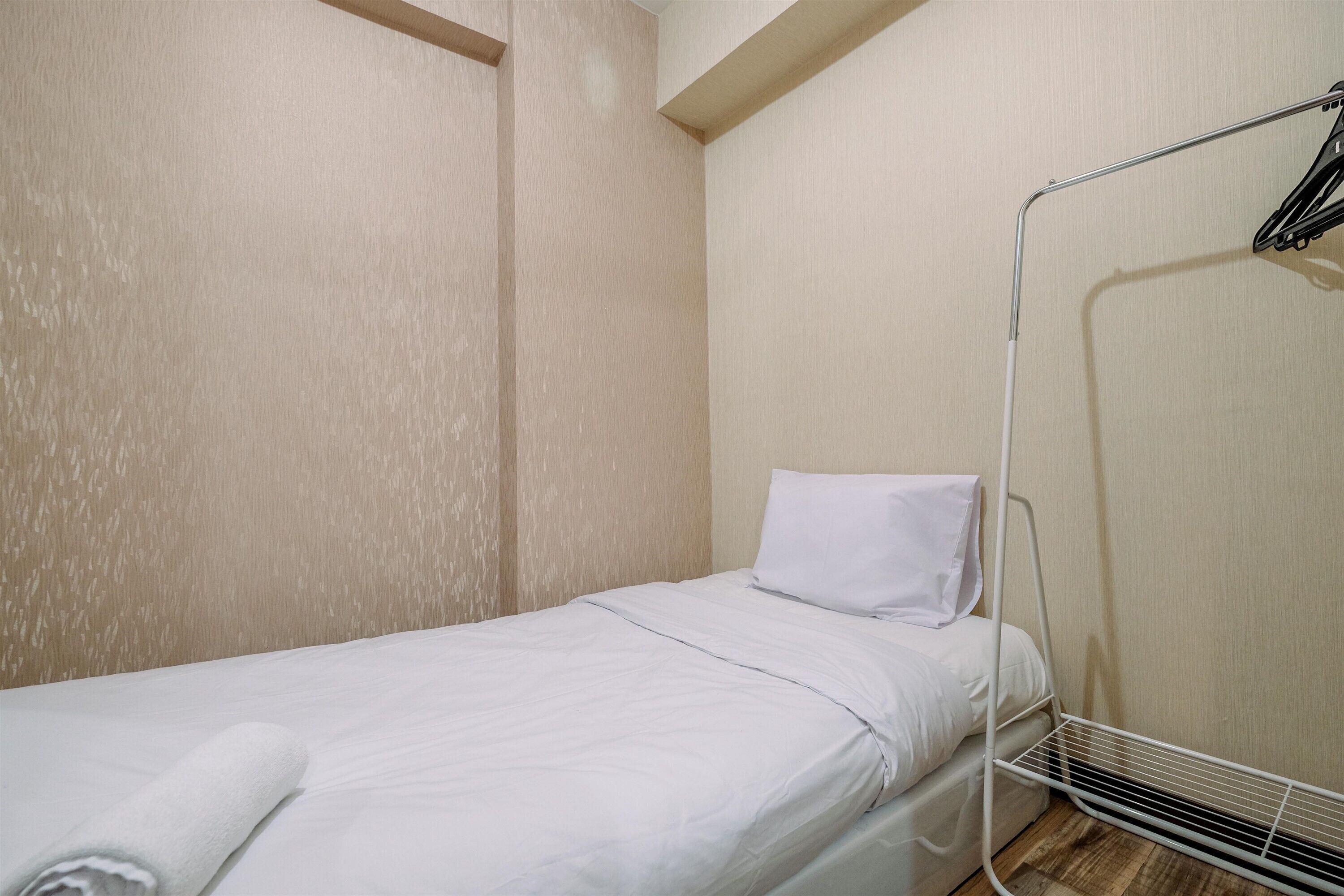 Una habitación pequeña con cama individual, ropa de cama blanca, una almohada y una toalla enrollada sobre la cama.