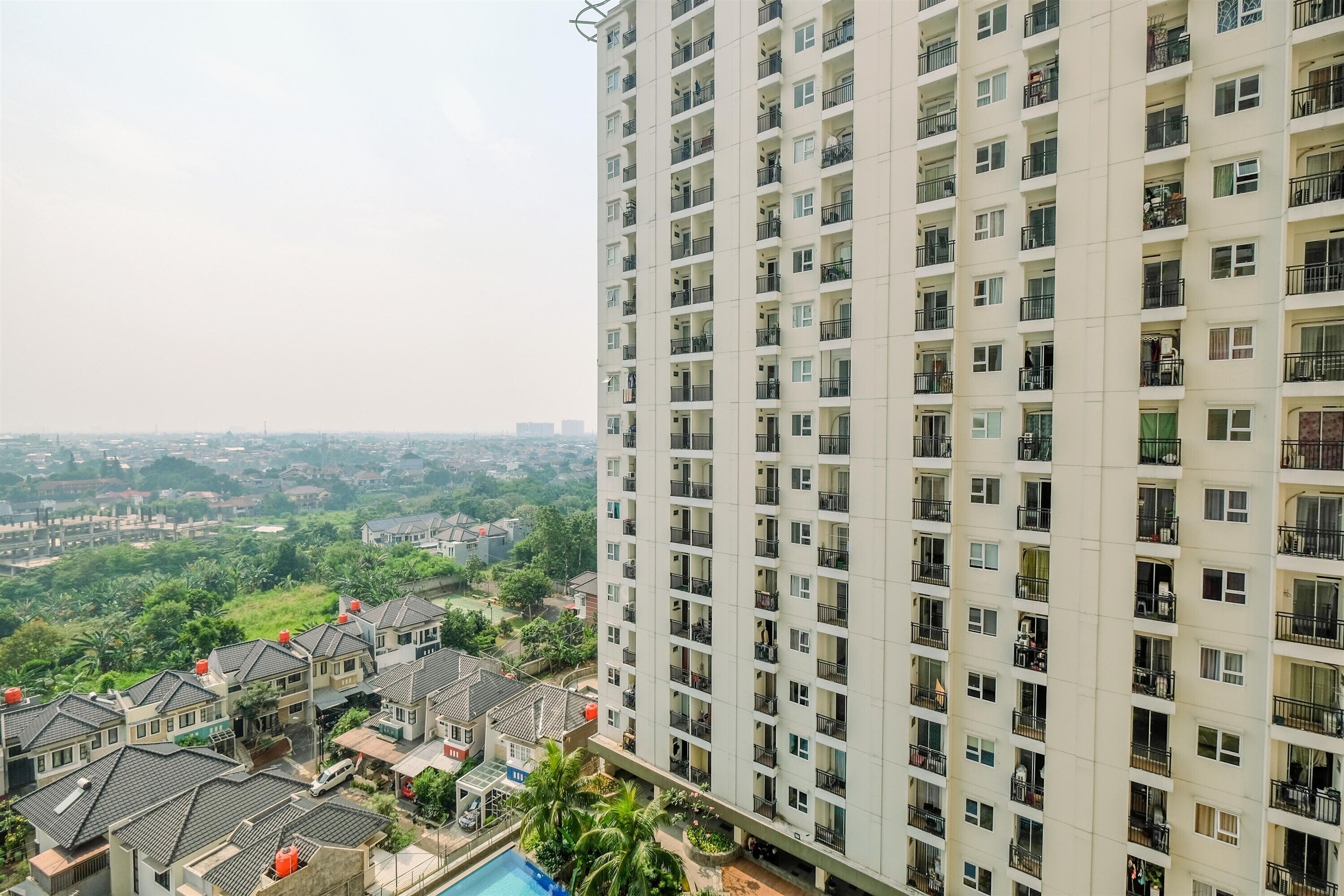 A high-rise residential building with multiple balconies and a view of a residential area with houses and greenery.