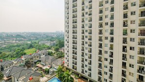 A high-rise residential building with multiple balconies and a view of a residential area with houses and greenery. - Homey And Simply 2Br Apartment At Cinere Resort (Depok)