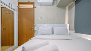 A hotel room with a bed, two wooden doors, a wall-mounted air conditioner, and a mirror. - Homey And Simply 2Br Apartment At Cinere Resort (Depok)