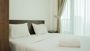 A hotel room with a bed, two pillows, a nightstand, and a window with curtains. - Nice And Elegant Studio At Tree Park City Apartment (South Tangerang)