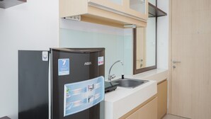 A compact kitchen with a black refrigerator, a sink, and wooden cabinets. - Nice And Elegant Studio At Tree Park City Apartment (South Tangerang)