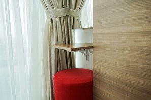 Ein spiegel mit Holzrahmen, ein roter Hocker und ein Fenster mit durchscheinenden Vorhängen.