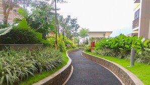 A curved pathway flanked by lush greenery and a brick wall, leading to a building with a visible entrance. - Comfy With Modern Style Springlake Summarecon Studio Apartment (Bekasi)