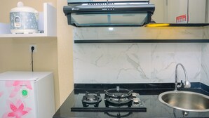 A kitchen with a gas stove, a sink, a microwave, and a water dispenser. - Comfy With Modern Style Springlake Summarecon Studio Apartment (Bekasi)