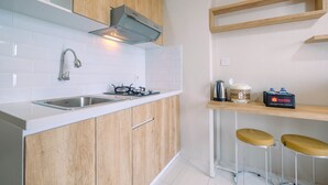 A modern kitchen with wooden cabinets, a stainless steel sink, and a gas stove. There are two stools and a shelf with a kettle and a travel bag. - Brand New Fabulous 2Br Podomoro Golf View Apartment By Travelio (Gunung Putri)