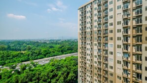 A high-rise building with multiple balconies, a view of a highway, and surrounding greenery. - Brand New Fabulous 2Br Podomoro Golf View Apartment By Travelio (Gunung Putri)