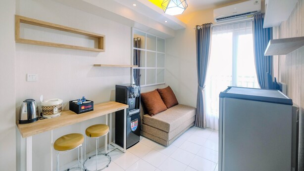 A compact hotel room with a kitchenette, a sofa bed, a small bar area, and a window with curtains. - Brand New Fabulous 2Br Podomoro Golf View Apartment By Travelio (Gunung Putri)