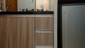 A kitchen with wooden cabinets, a stainless steel refrigerator, and a sink with a faucet. - Cozy With Good Location Studio At Tifolia Apartment By Travelio (Jakarta)