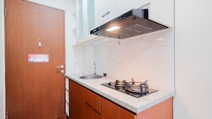 A compact kitchen with a wooden door, a stainless steel sink, a gas stove, and a black range hood. - Cozy And Simply Studio Tifolia Apartment Near Kelapa Gading By Travelio (Jakarta)