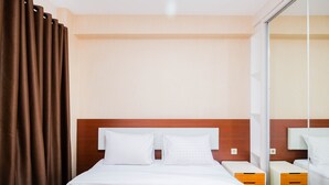 A hotel room with a large bed, two bedside tables, a mirror, and brown curtains. - Cozy And Simply Studio Tifolia Apartment Near Kelapa Gading By Travelio (Jakarta)