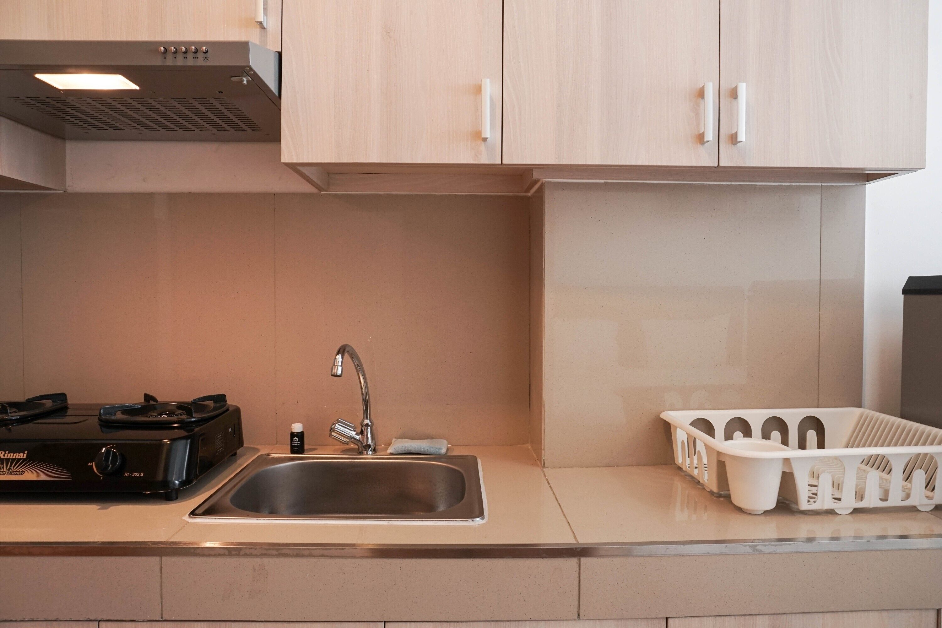 A kitchen with a stainless steel sink, a gas stove, and light wooden cabinets.
