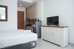A bedroom with a bed, a television on a wooden cabinet, a refrigerator, and a wooden door.