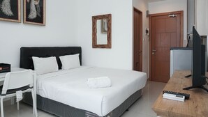 A hotel room with a bed, a desk, a chair, a TV, and a door. - Relax Studio Apartment At The Nest Near Puri By Travelio (Tangerang)