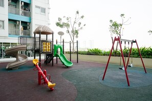Children can play on the slide, seesaw, and swing set in this outdoor play area surrounded by greenery.