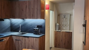 A compact kitchen with wooden cabinets, a black countertop, a sink, a coffee machine, and a small dining area with wooden chairs. - Renovated triplex apt for 7 in Avoriaz, terrace, ski locker (Avoriaz)