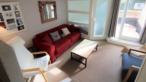 A living room with a red sofa, a white armchair, a wooden coffee table, and a large window with a view of the outdoors. - Renovated triplex apt for 7 in Avoriaz, terrace, ski locker (Avoriaz)