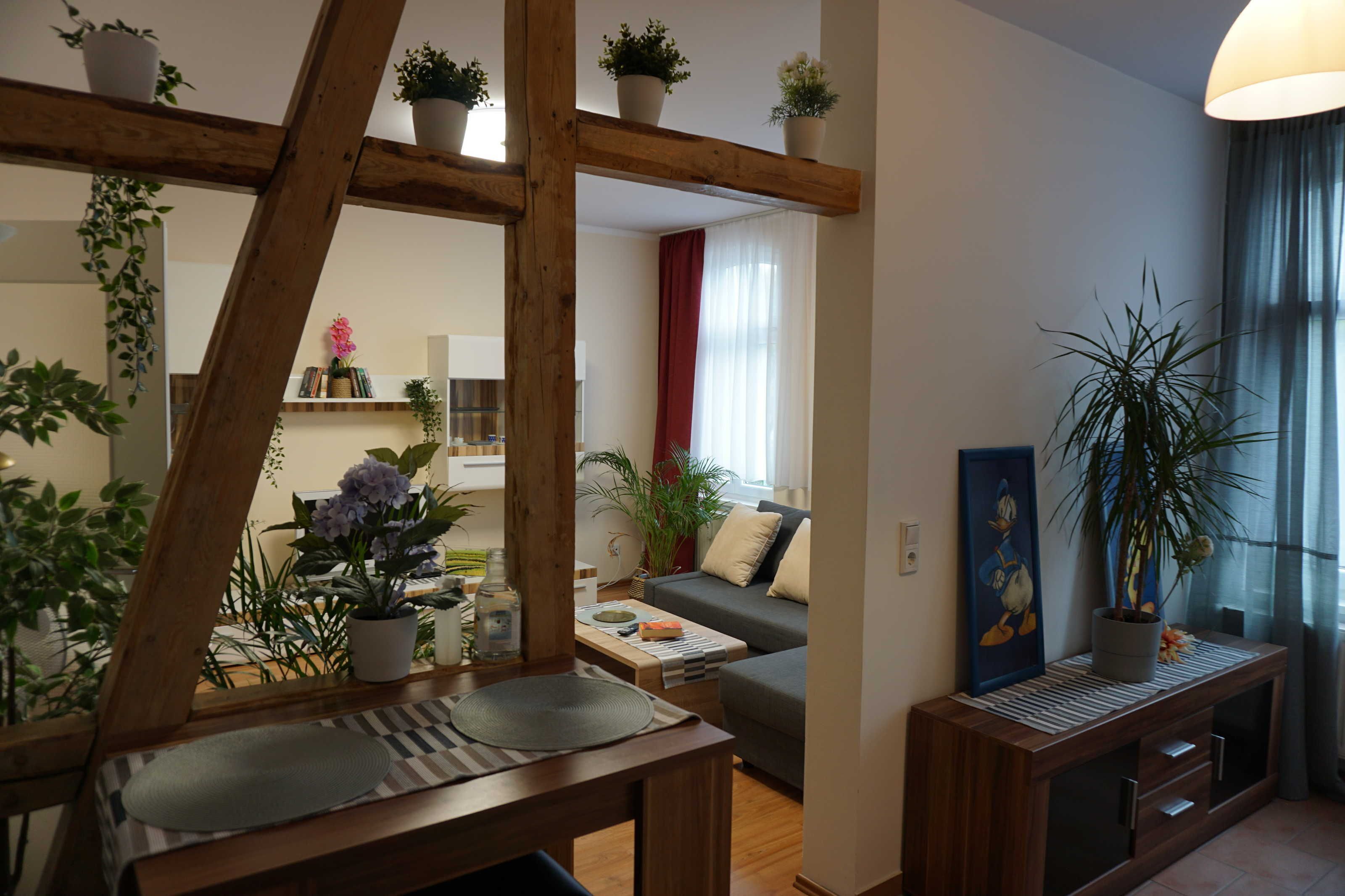 A living room with a wooden beam structure, a sofa, a coffee table, and various potted plants.