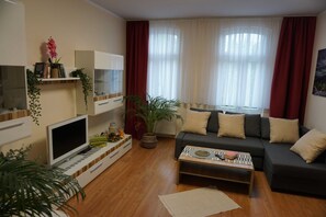 A living room with a sofa, coffee table, TV, and a plant.