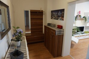 Una habitación con un armario de madera, un tapete a rayas, una planta en maceta y un cuadro con una vista urbana en la pared.