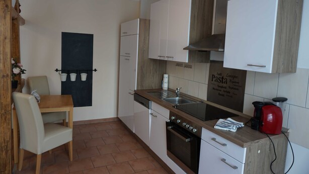 A compact kitchen with white cabinets, a wooden countertop, a built-in oven, and a blackboard with Italian pasta names. - Poldi 3 - Apartments Poldi (Erfurt)