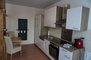A compact kitchen with white cabinets, a wooden countertop, a built-in oven, and a blackboard with Italian pasta names. - Poldi 3 - Apartments Poldi (Erfurt)