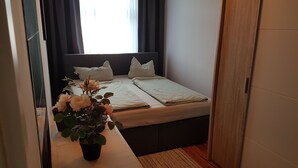 A bedroom with a bed, pillows, a bedside table with a potted plant, and a window with curtains. - Poldi 3 - Apartments Poldi (Erfurt)
