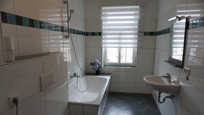 A bathroom with a bathtub, a sink, and a window with blinds. - Poldi 3 - Apartments Poldi (Erfurt)