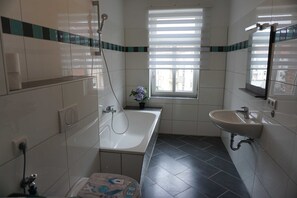 A bathroom with a bathtub, a sink, and a window with blinds. - Poldi 3 - Apartments Poldi (Erfurt)