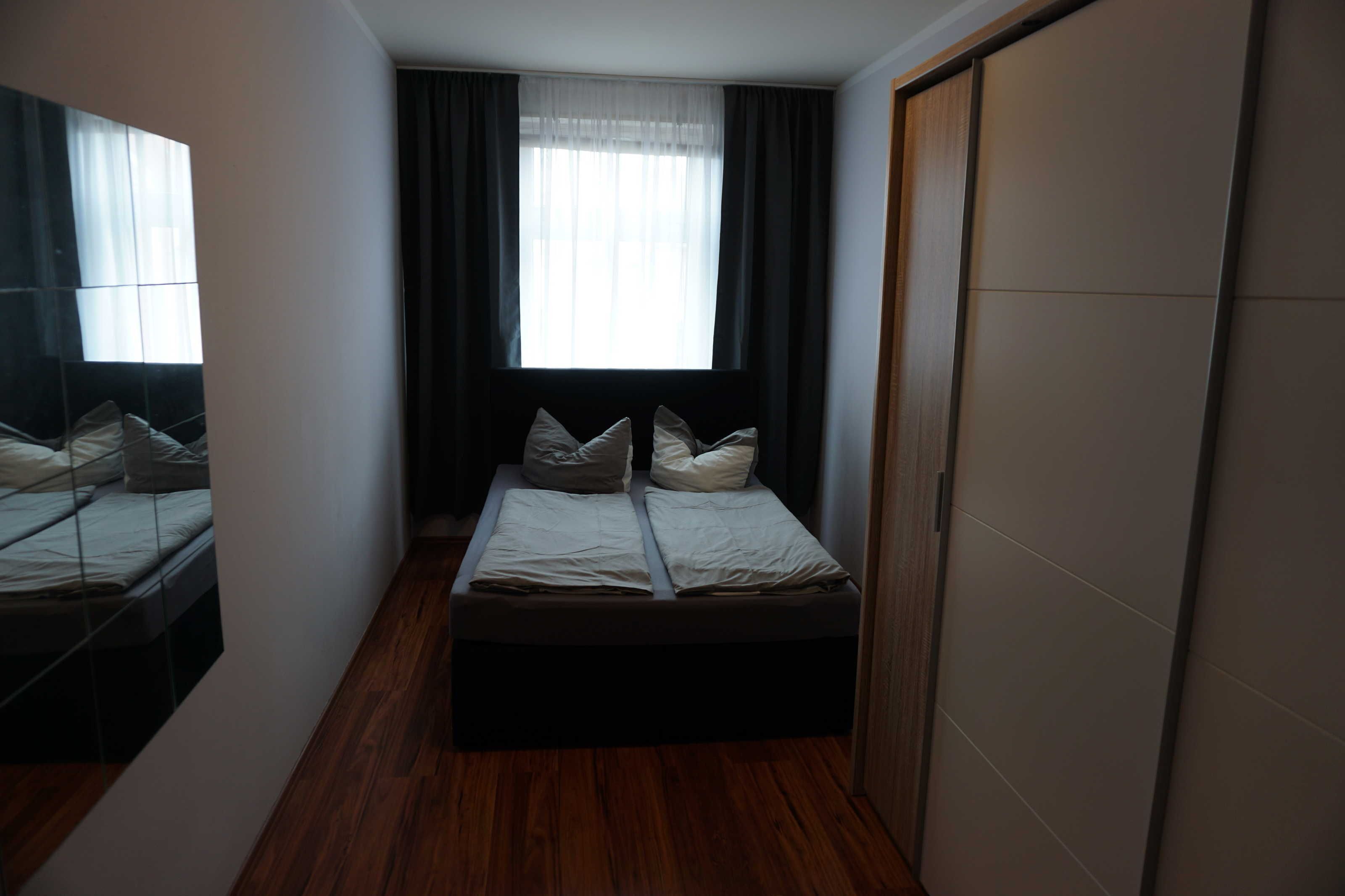 Un dormitorio con cama, espejo, ventana con cortinas y armario.